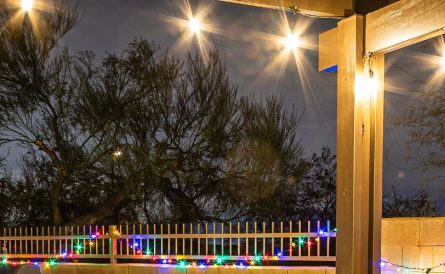 A Patio Cover And Fence Strung With Holiday Lights
